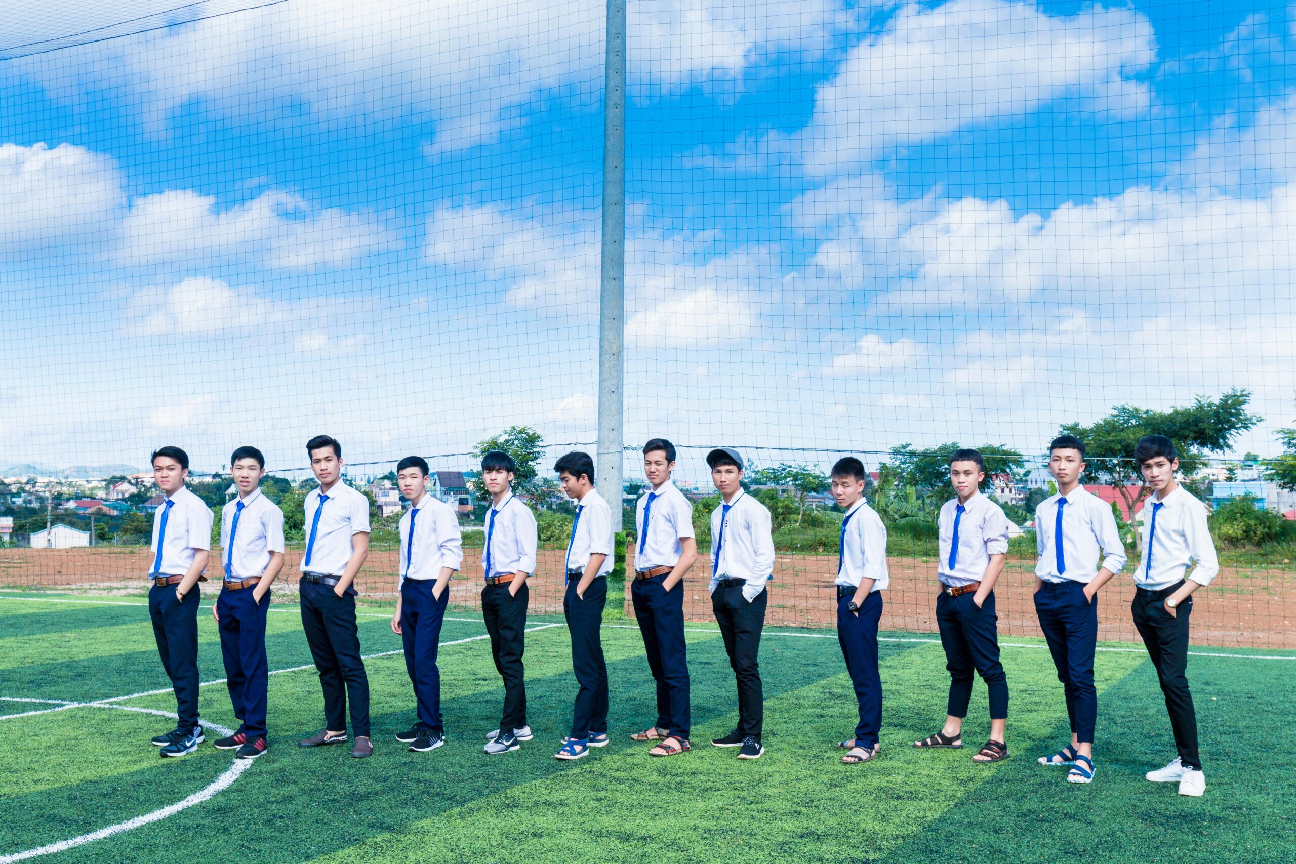 A group of young men in uniforms pose confidently on a soccer field under a clear blue sky.