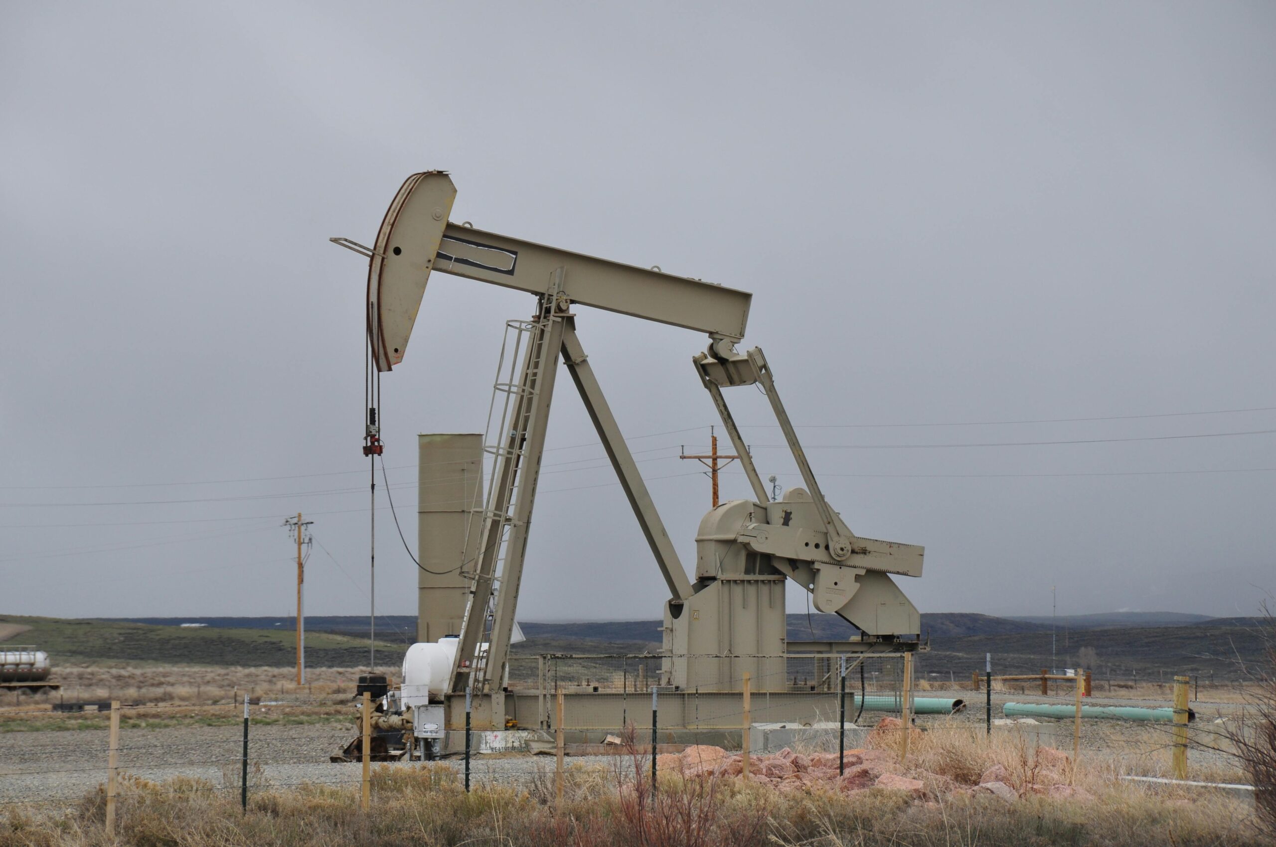 Oil pumpjack surrounded by barren landscape under overcast skies, showcasing industrial machinery.