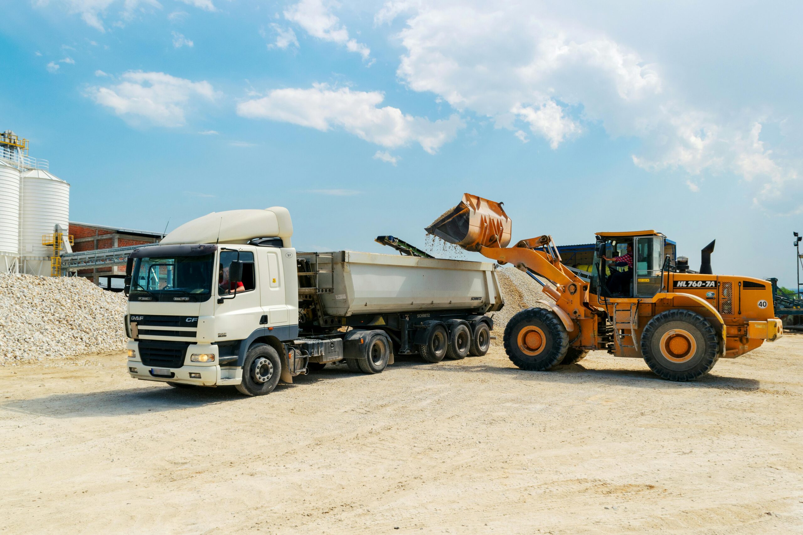 Excavator loading materials into a heavy-duty truck at a sunny construction site.