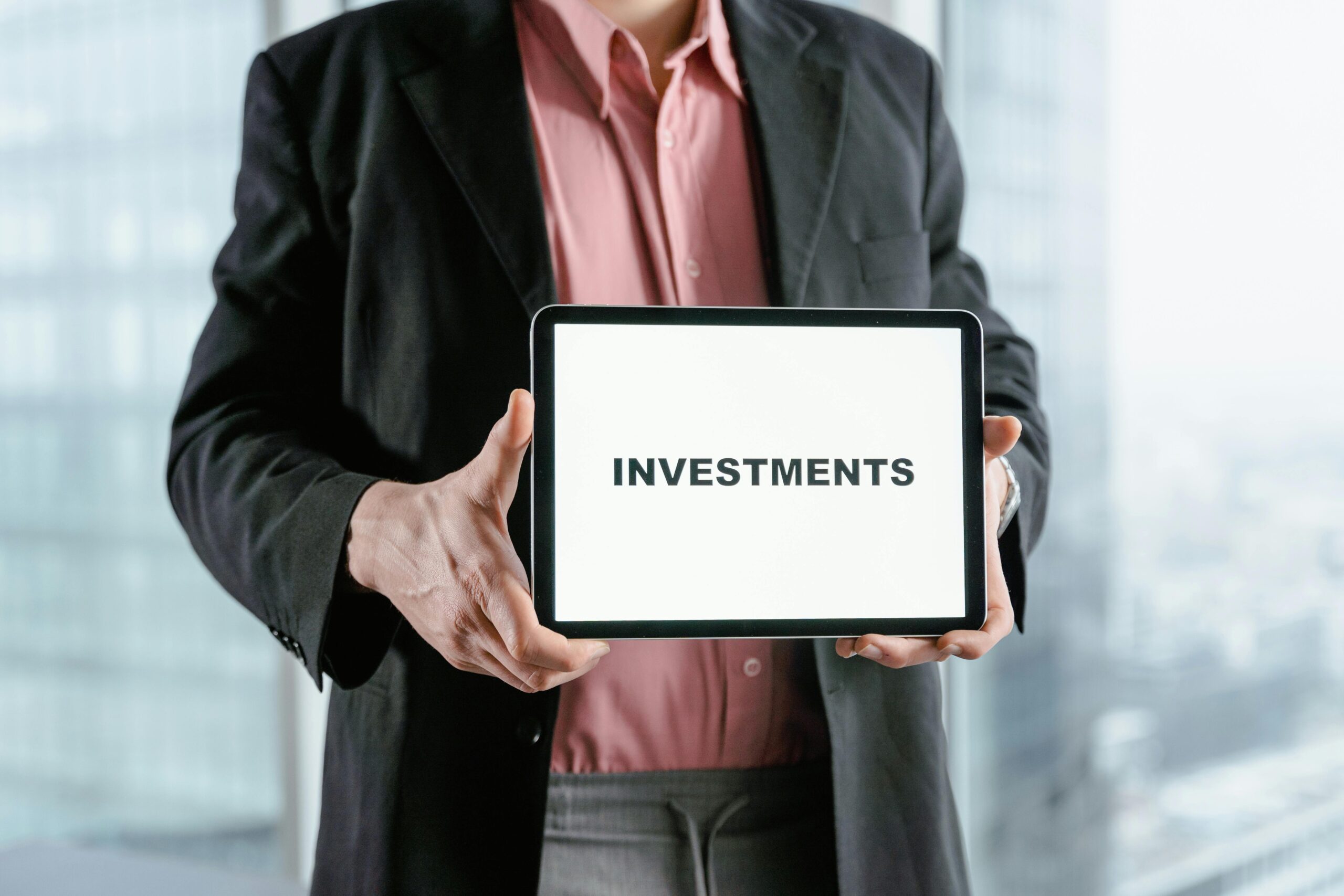 Professional holding a tablet with 'INVESTMENTS' text, ideal for finance and business themes.